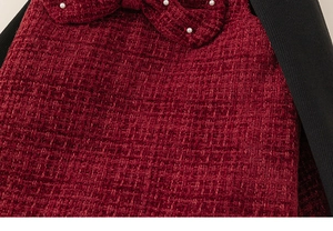 Close-up of red tweed fabric featuring a bow detail with white pearls and black knit ribbing