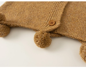 Close-up of ochre knit cardigan fabric featuring plush pom-poms and round button detail