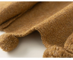 Macro shot of yellow knit cardigan showing thick textured yarn and cute pom-poms