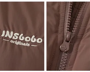 Détail du gilet matelassé marron montrant la broderie blanche et la fermeture éclair