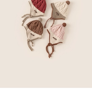 Detailed view of knitted toddler earflap hats in four soft colors with pom-poms