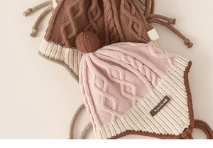 Close-up of cable knit texture on toddler earflap hats with braided ties and pom-poms