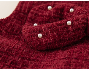 Detail of red bouclé fabric with elegant white pearl accents on the girl costume