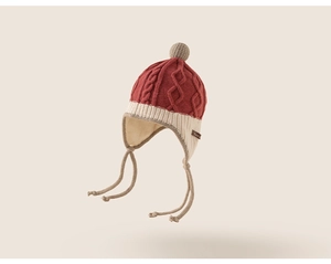 Detail of cable knit kids earflap hat in brick red with pompom and braided ties