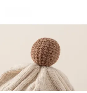 Detailed macro view of beige knit baby hat featuring a dark brown woven pompom on top