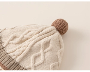 Close-up of knit toddler hat with thick cable weave pattern and brown fluffy pompom