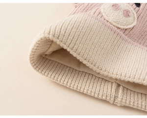 Detailed close-up of pink and beige knitted baby hat with soft inner lining and pig embroidery