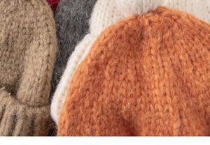 Detailed macro view of soft knit texture and pom-poms on assorted children winter hats
