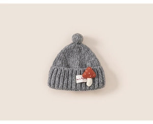Close-up of grey baby knit hat featuring a mushroom patch and fluffy pom-pom detail