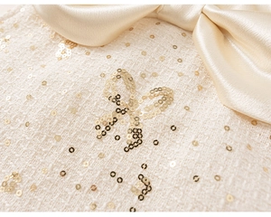 Detailed view of cream tweed dress with silk satin bow and sparkling gold sequins