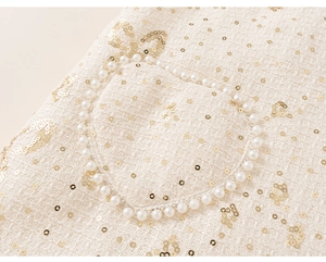 Detailed macro view of white tweed fabric with pearl pocket and gold sequin patterns