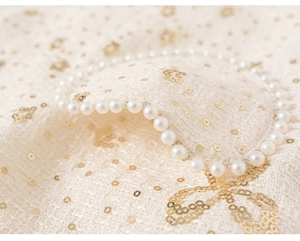 Close-up of cream tweed fabric with golden sequins, bow patterns and pearl trim detail