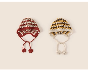 Close-up of handmade crochet baby earflap hats with cute flower tassels and striped patterns