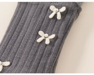 Détail de legging en tricot gris foncé avec nœud en ruban crème et perle nacrée