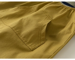 Detail of mustard yellow cotton trousers featuring elastic waist and double-stitched cargo pocket
