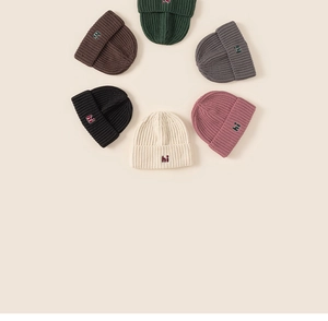 Flat lay of ribbed knit kids beanies in six colors with simple 'hi' embroidery