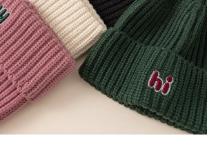 Detailed close-up of knitted beanies with hi embroidery in pink, black and green