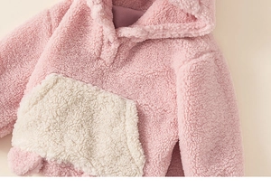 Détail de sweat à capuche rose en polaire pour enfant avec poche blanche et bouton