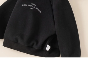 Close-up of boys' fleece hoodie rib-knit hem and white graphic print on black fabric
