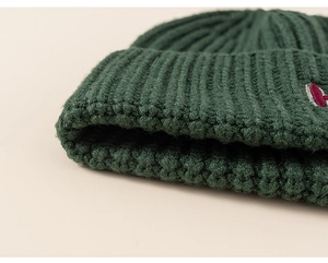 Close-up of dark green ribbed knit texture and embroidered patch on winter beanie