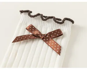 Close-up of white knit kids socks featuring brown polka dot bows and ruffled edges