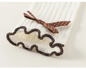 Detail of white ribbed knit socks with brown ruffle edge and polka dot satin bow decoration
