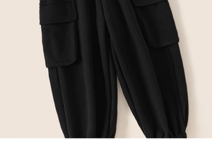 Detail view of black cargo pants featuring large flap side pockets and elastic ankle cuffs