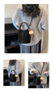 Detail view of black suede bucket bag featuring contrast stitching and plush dog charm