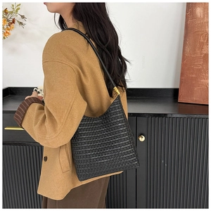Détail d'un sac cabas tissé noir vintage porté avec une bandoulière chic et des finitions