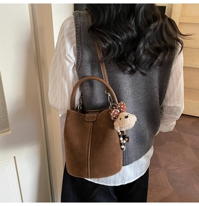 Detail of dark brown suede bucket bag with cute bear charm worn by a model in casual style
