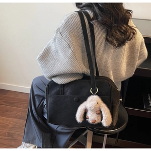 Detail of black leather tote bag with a cute plush rabbit charm on a stylish shoulder strap