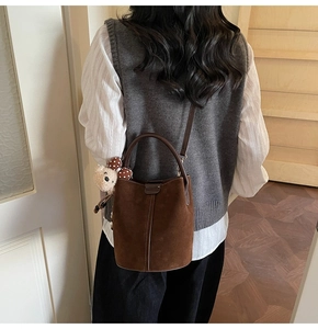 Macro shot of dark brown suede bucket bag with cute teddy bear charm on model back