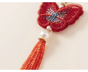 Détail du papillon brodé rouge avec des accents de perles et des glands de perles orange