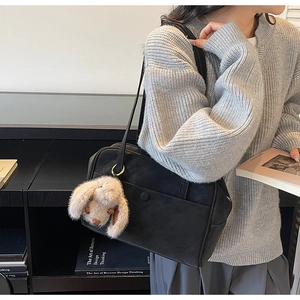 Detail of minimalist black leather shoulder bag with a cute beige plush bunny keychain
