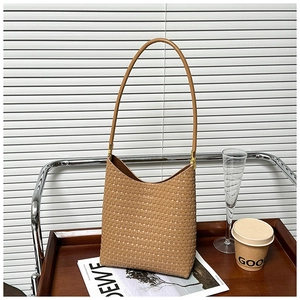 Khaki woven leather shoulder bag displayed on a wooden tray with soft window lighting