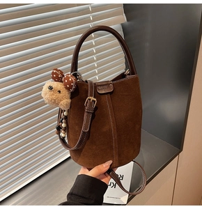 Detail of dark brown suede bucket bag featuring a cute teddy bear charm and top handle