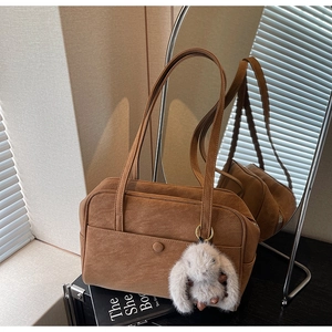 Brown suede pillow bag with a plush rabbit charm shown in a cozy studio setting