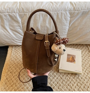 Detail view of brown suede bucket bag featuring embossed logo and a plush bear charm