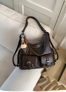 Detail of dark brown leather hobo bag with two buckle pockets and plush charm