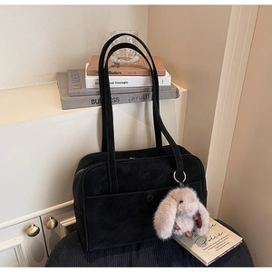 Close-up of black suede shoulder bag with rabbit charm and front pocket detail