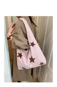 Detail view of pink knit tote bag with brown star pattern worn by a model in soft lighting