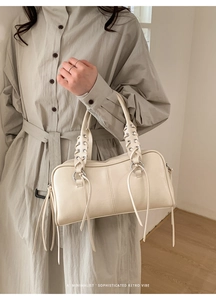 Detail view of woven top handles and decorative hanging leather straps on off-white handbag