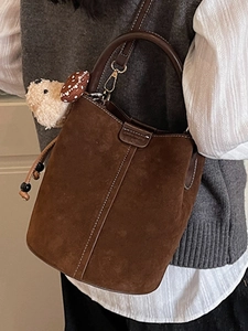 Retro brown suede bucket bag with decorative stitching and cute plush bear charm