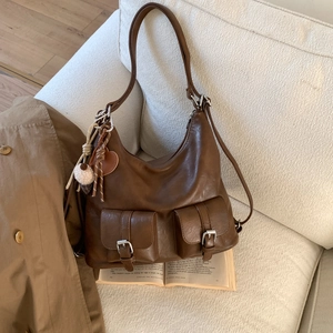 Detail of dark brown vintage Hobo bag with dual front pockets and heart charm on a sofa