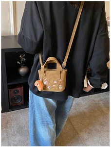 Détail d'un sac bandoulière marron avec broderie et un joli pendentif pain peluche