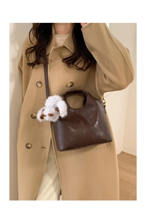 Detail of vintage dark brown leather bucket bag with a cute white plush dog charm