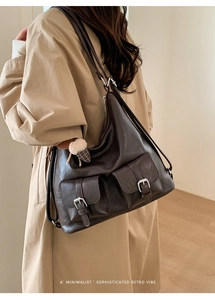 Close-up of retro brown leather shoulder bag featuring metal buckles and plush charm