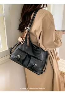 Detail of retro black leather tote bag with buckle pockets worn with a beige trench coat
