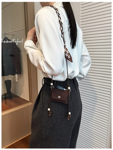 Detail of a mini brown suede crossbody bag featuring a printed silk scarf and decorative beads
