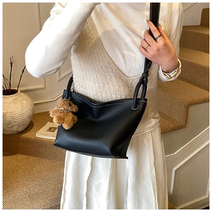 Détail du sac seau en cuir noir avec surpiqûres blanches et charm d'ours peluche